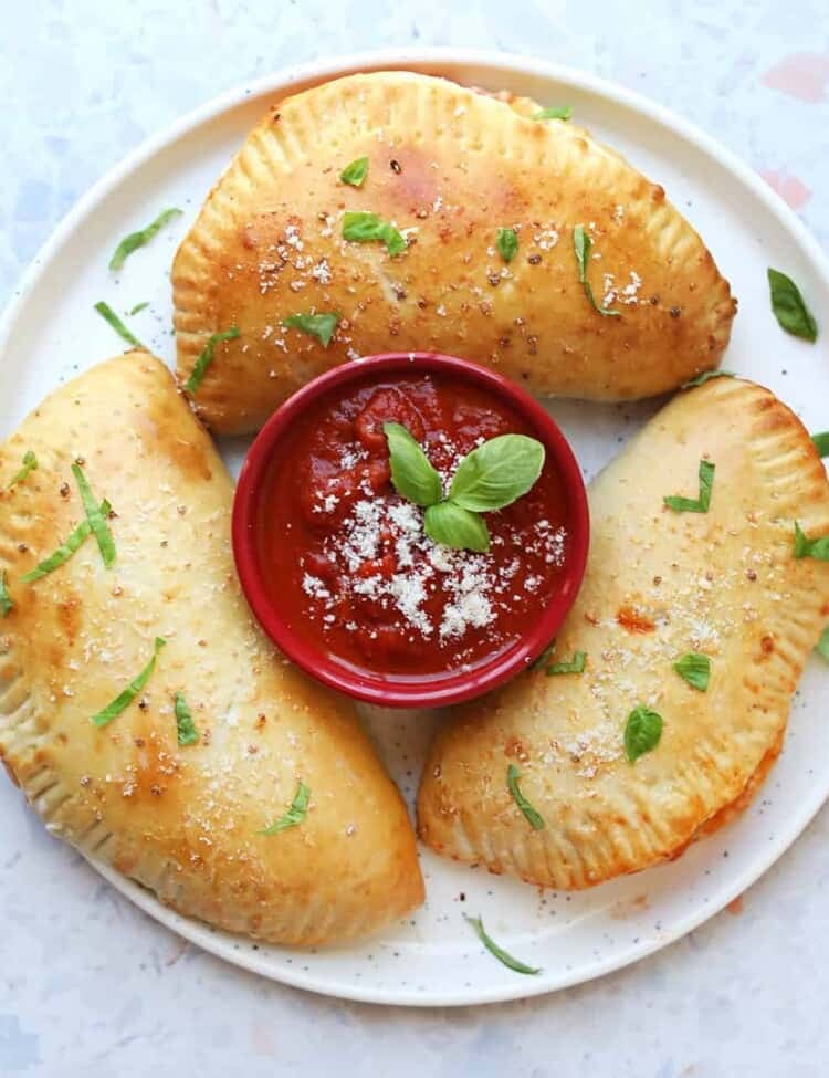 three calzones on a plate with red sauce